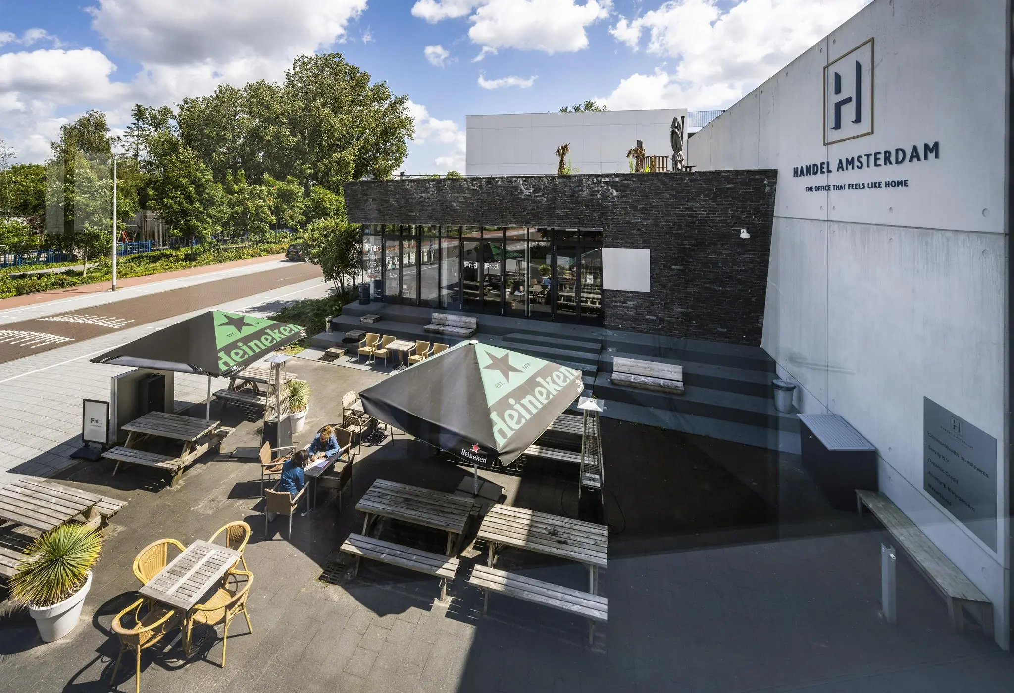 Terras met picknicktafels en Heineken-parasols bij het moderne kantoorgebouw Handel Amsterdam aan de Fred. Roeskestraat.